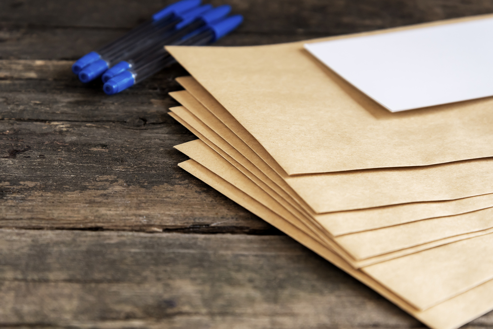 Pile,Of,Post,Envelopes,And,Blue,Pens Enveloppes en papier kraft symbolisant la hausse des tarifs postaux